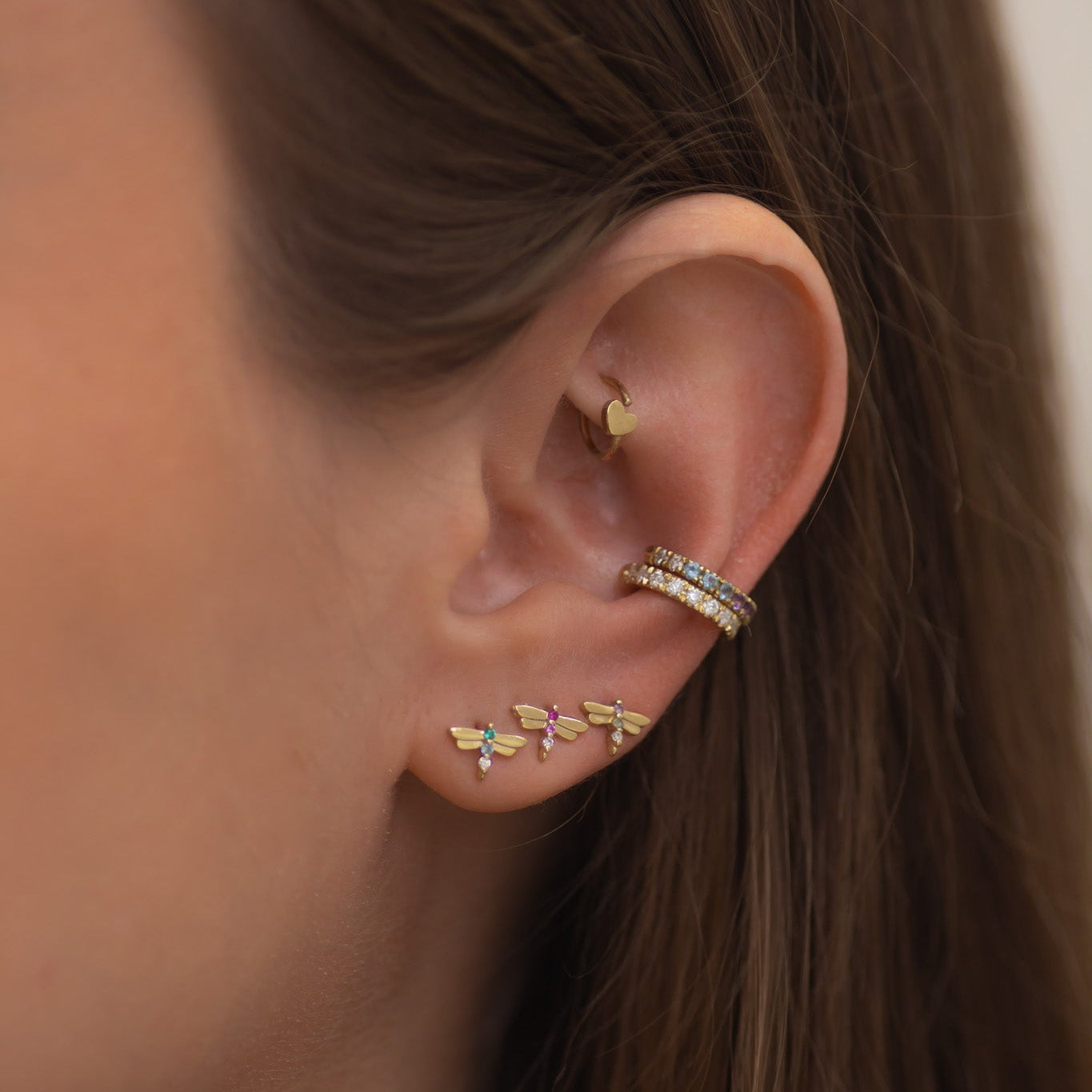 Close-up of an ear with gold earrings and a ring, against a neutral background